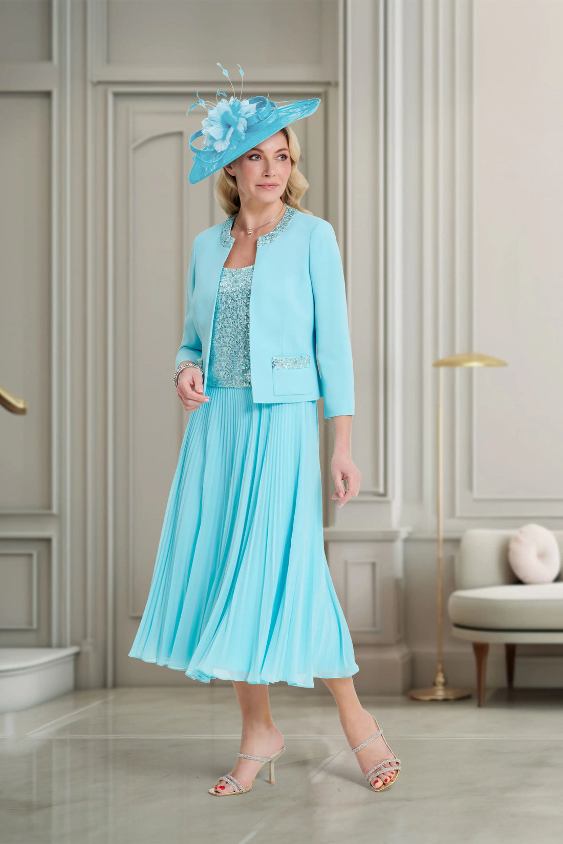 Woman in a light blue dress and jacket with a matching hat in an elegant room.