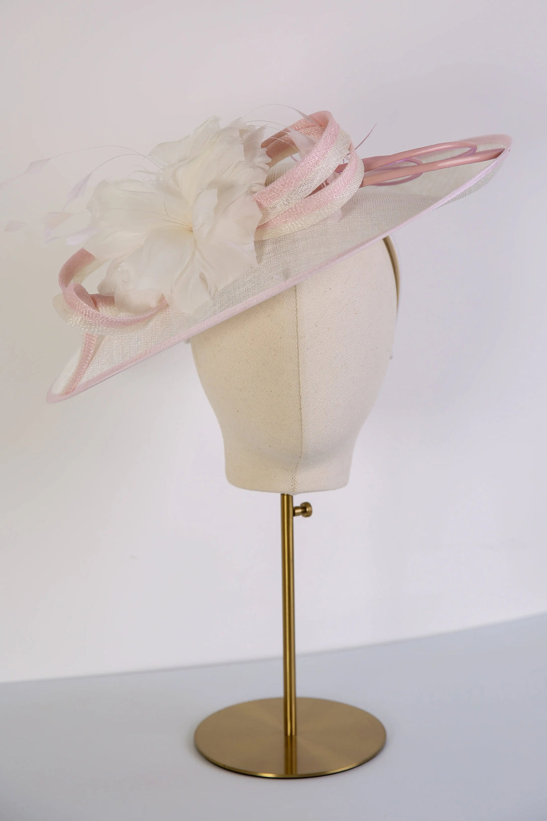 Pink and white decorative hat on a mannequin head with a white background