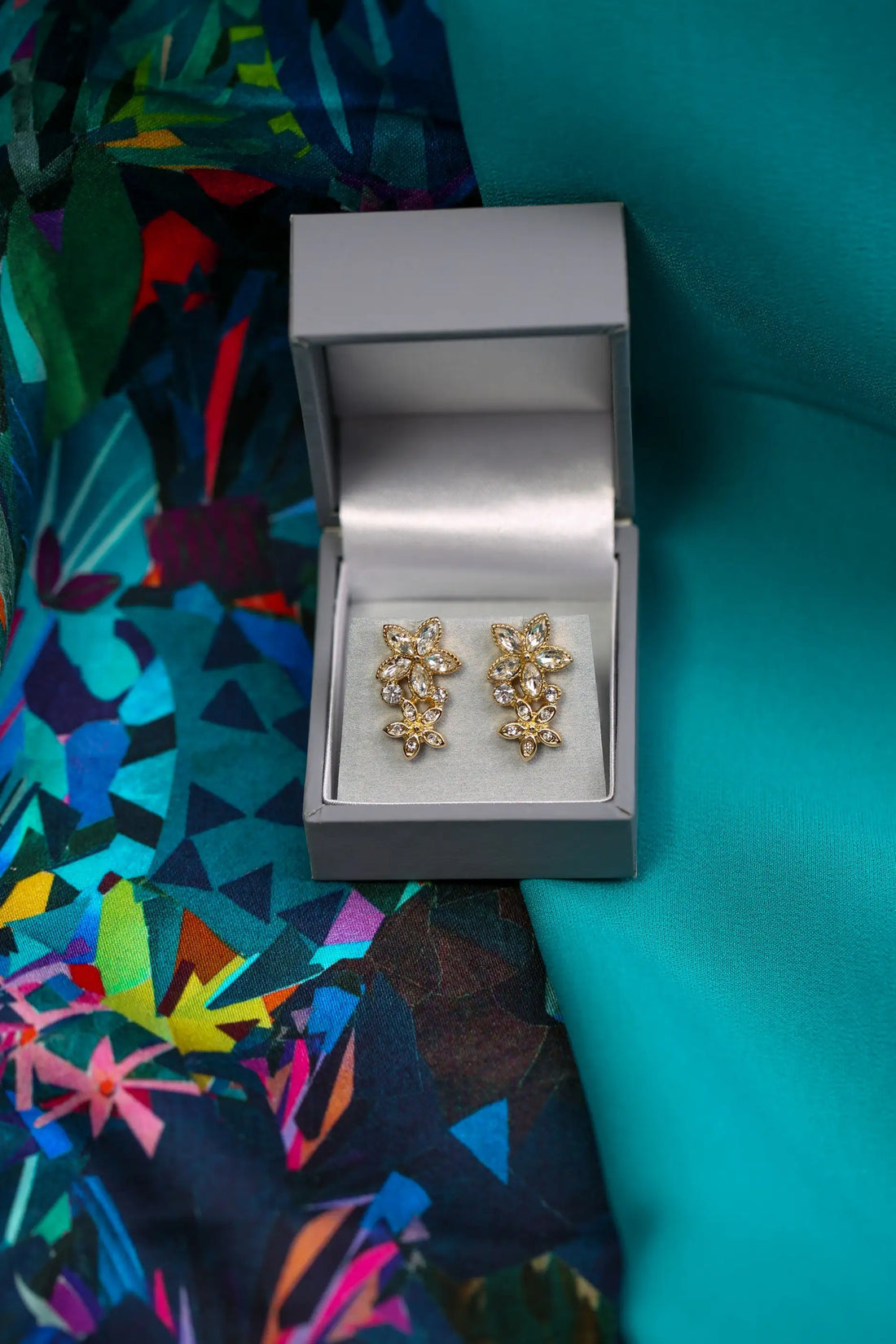 Gold floral earrings in a silver box on a colorful fabric background