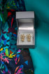 Gold floral earrings in a silver box on a colorful fabric background
