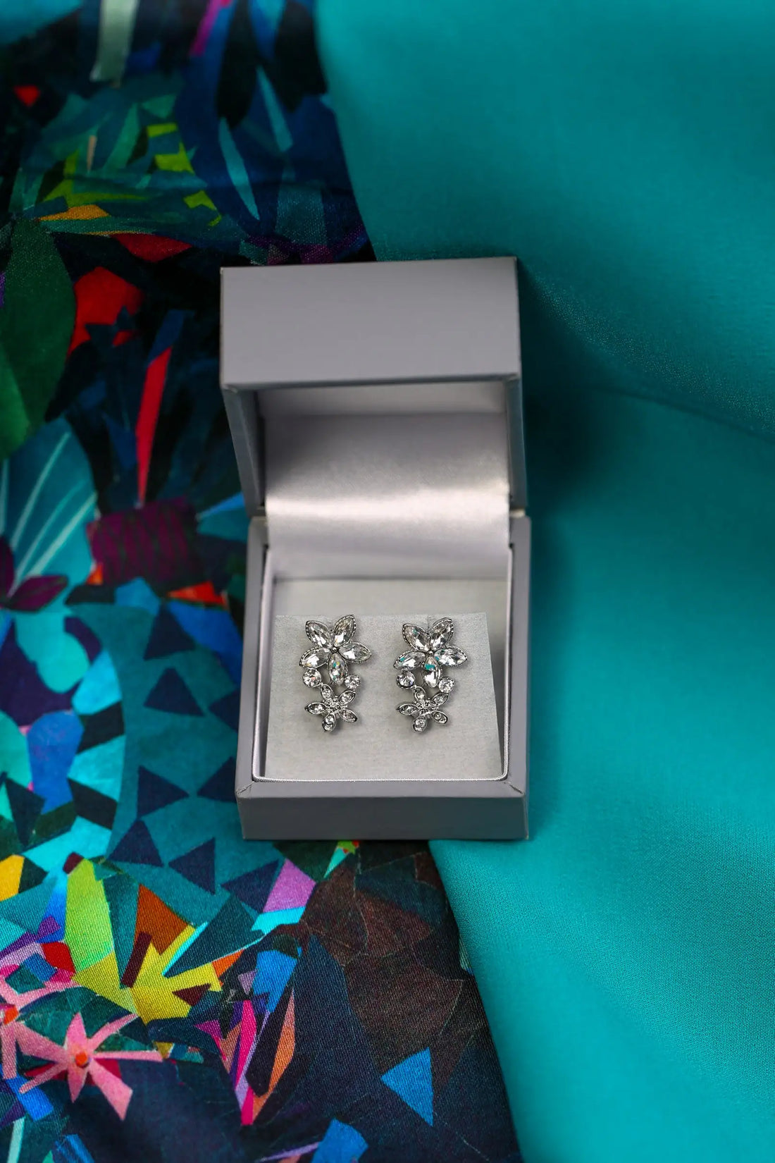Silver earrings in a box on a colorful fabric background