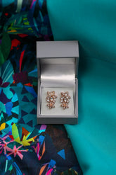 Rose gold earrings in a silver display case on a colorful fabric background