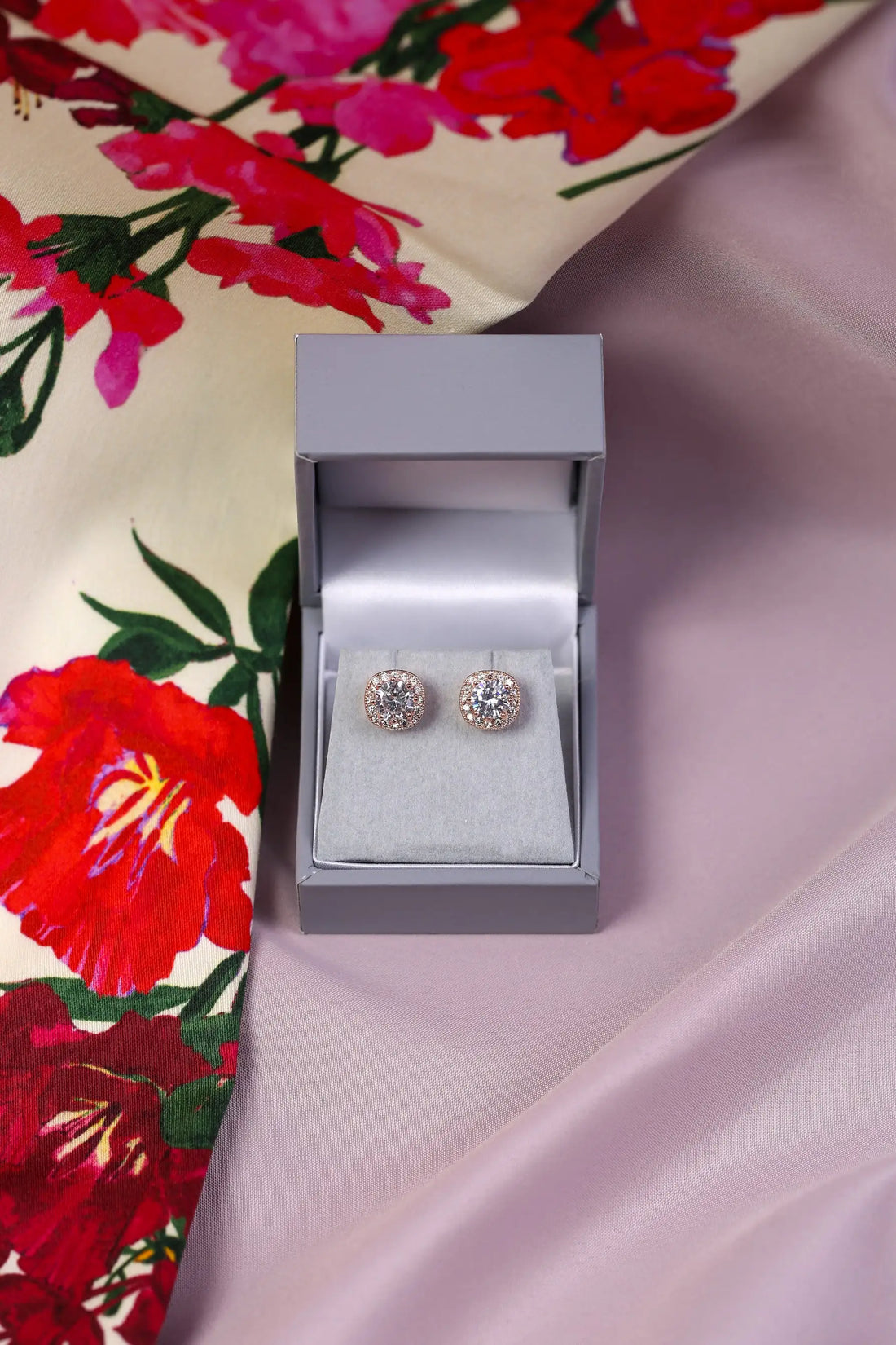 A pair of crystal halo stud earrings displayed in an open grey box, with the earrings themselves having a large central clear crystal surrounded by smaller clear crystals.