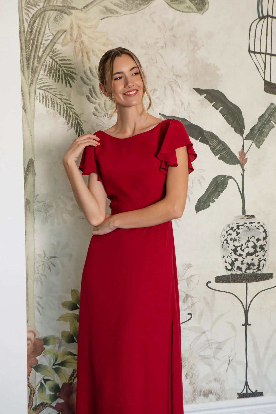 Woman wearing a red dress with ruffled sleeves against a decorative wall.