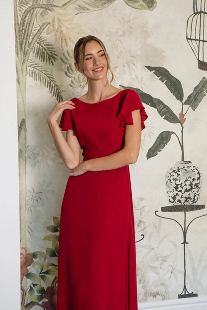 Woman wearing a red dress with ruffled sleeves against a decorative wall.