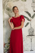 Woman wearing a red dress with ruffled sleeves against a decorative wall.
