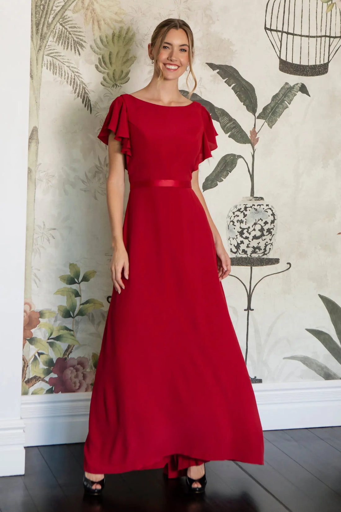 Woman wearing a red dress with ruffled sleeves against a decorative wall.