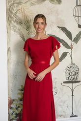 Woman wearing a red dress with ruffled sleeves against a decorative wall.
