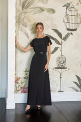 Woman in a black dress standing against a decorative wall with floral and birdcage designs.