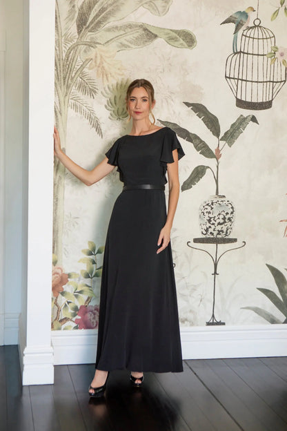 Woman in a black dress standing against a decorative wall with floral and birdcage designs.