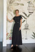 Woman in a black dress standing against a decorative wall with floral and birdcage designs.