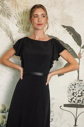 Woman wearing a black dress with ruffled sleeves against a decorative wall.