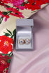 A pair of crystal earrings in a gold setting, presented in an open luxury box on a floral patterned fabric.