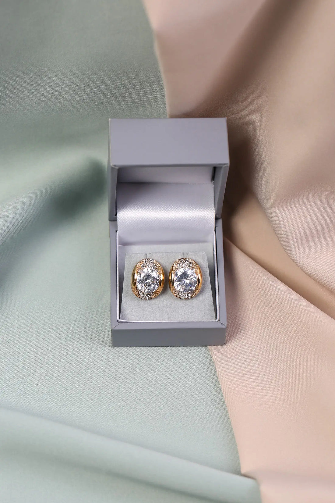 A pair of crystal earrings in a gold setting, presented in an open luxury box.
