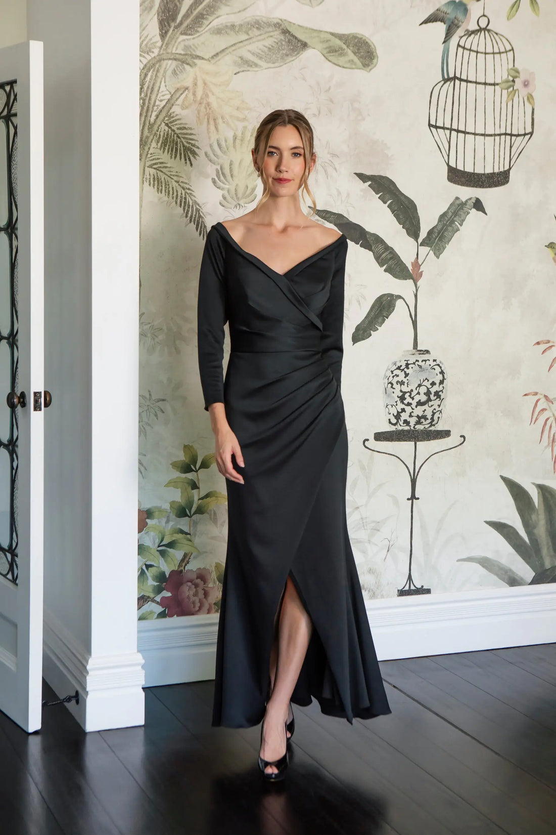 Woman in a black evening gown standing in front of a decorative wall with floral patterns.