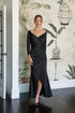 Woman in a black evening gown standing in front of a decorative wall with floral patterns.