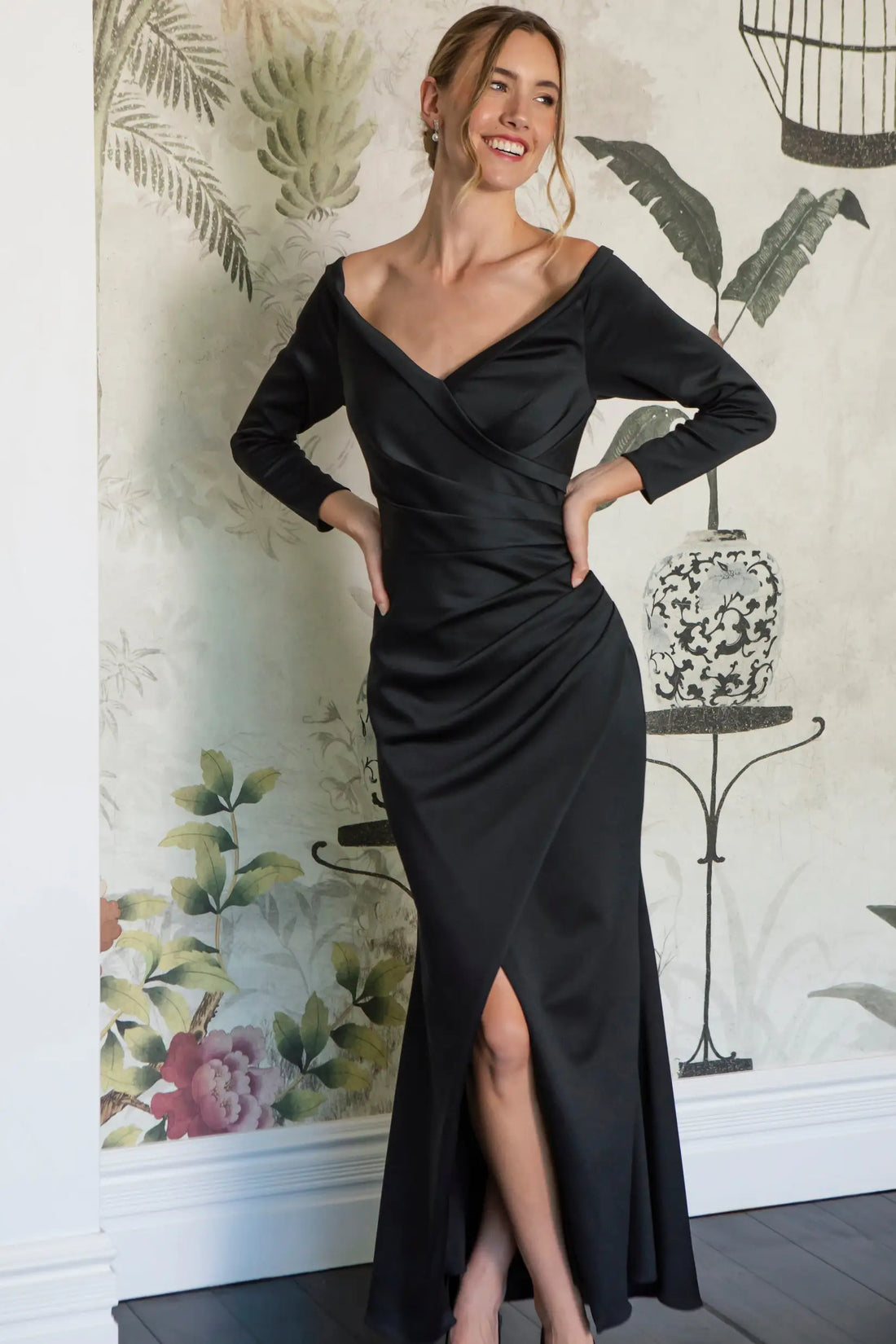 Woman wearing a black evening gown standing against a decorative wall.