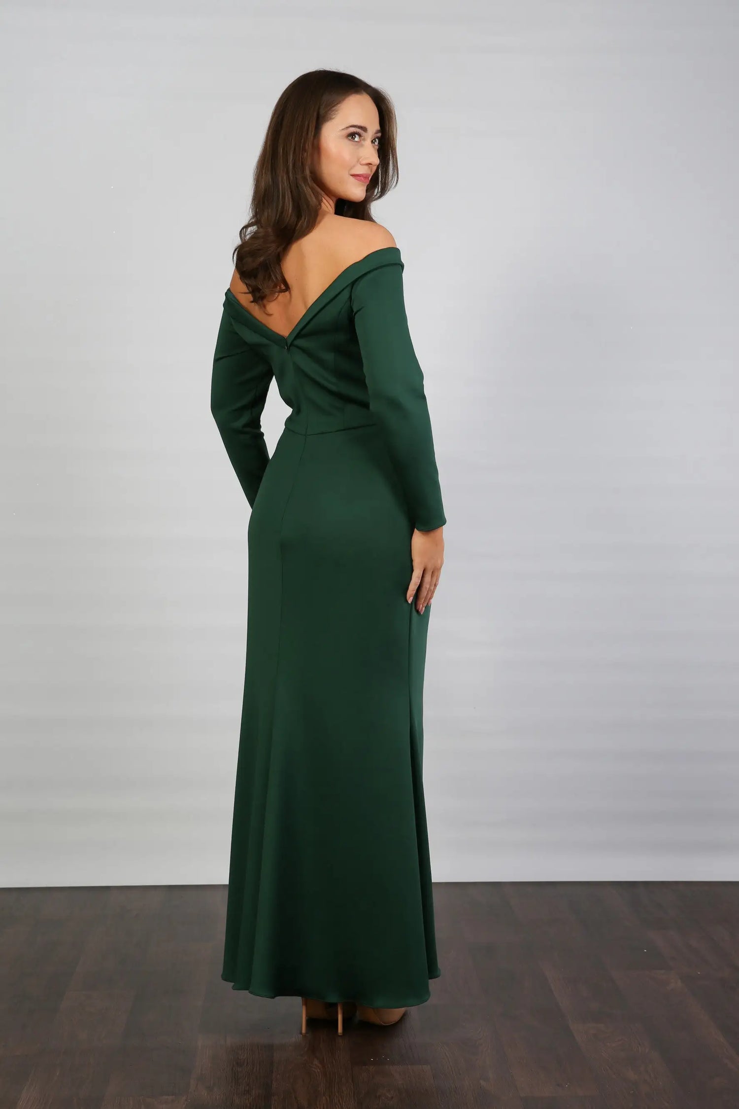 A woman models an off-the-shoulder, long-sleeved, green stretch jersey evening dress.