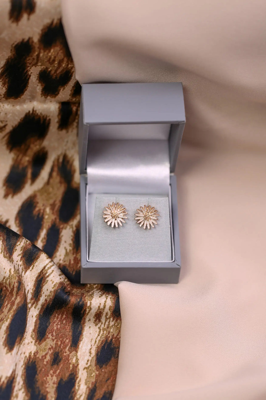 Pair of gold floral earrings in a grey jewellery box on a leopard print fabric background