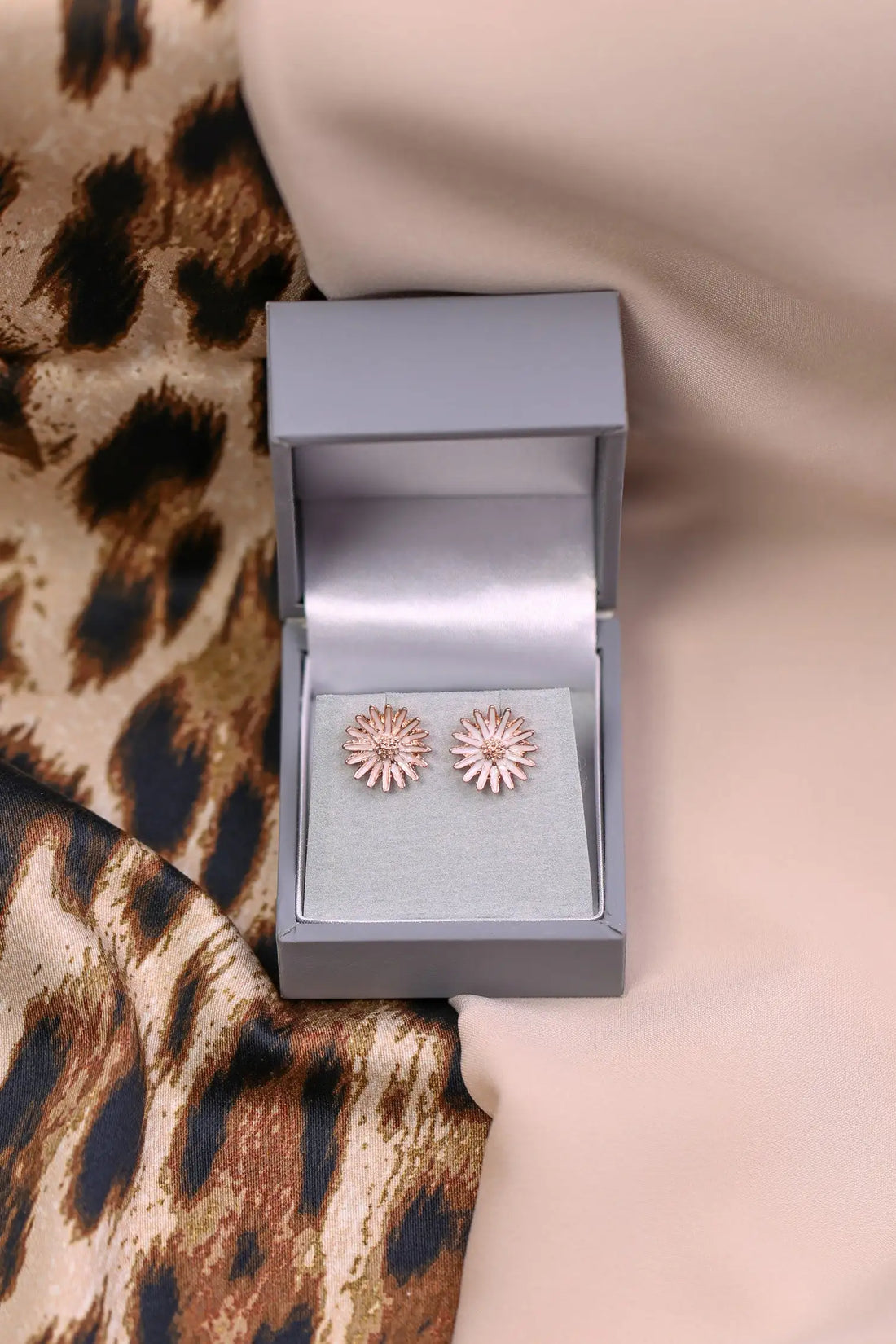 Rose gold floral earrings in an open jewellery box on a leopard print fabric background