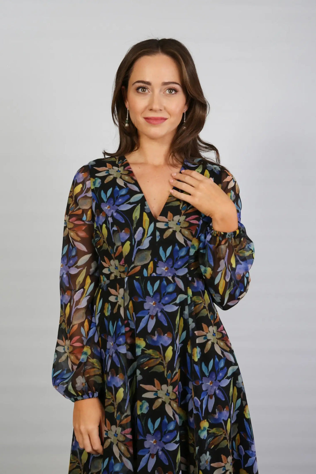 A woman standing indoors wearing a floral printed chiffon midi dress with long sleeves and a round neckline.