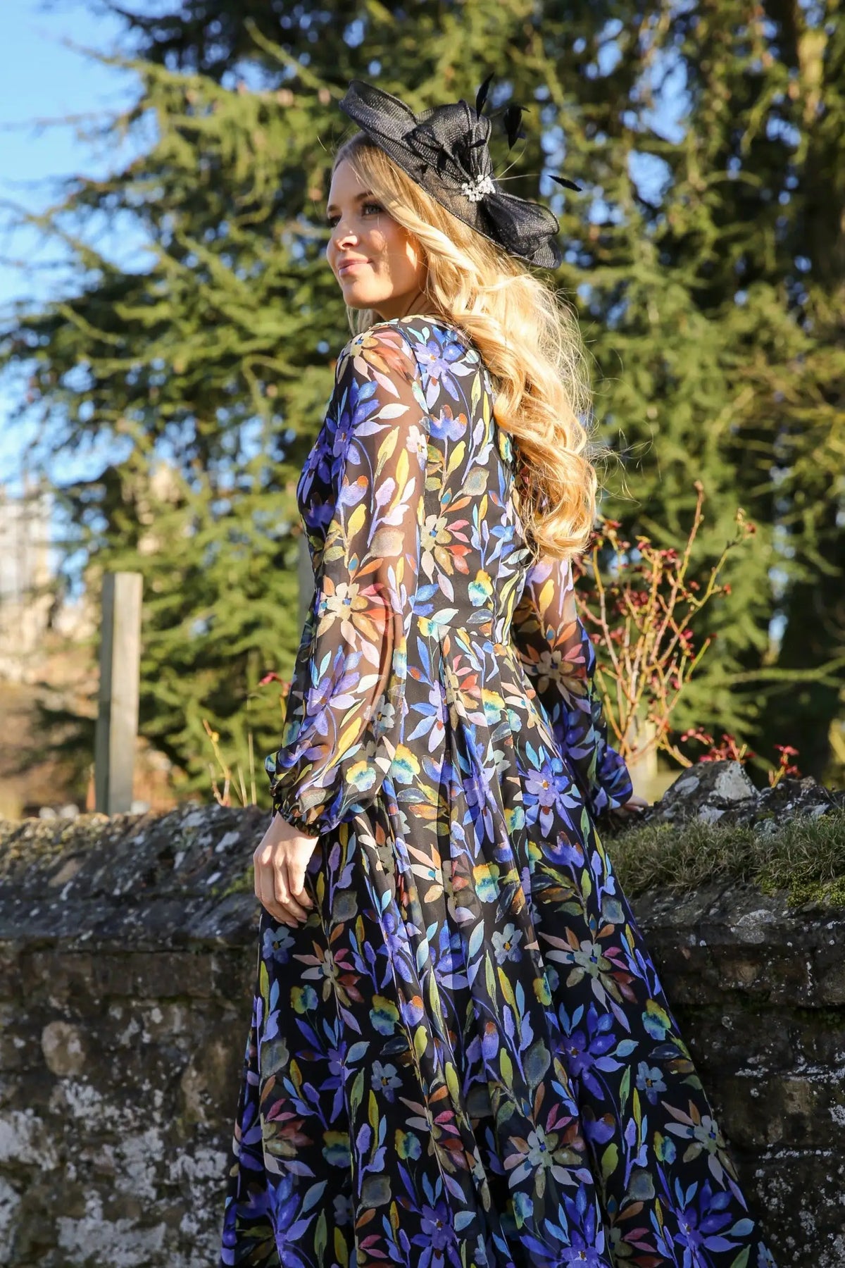 A woman standing outdoors wearing a floral printed chiffon midi dress with long sleeves and a round neckline.