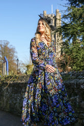 A woman standing outdoors wearing a floral printed chiffon midi dress with long sleeves and a round neckline.
