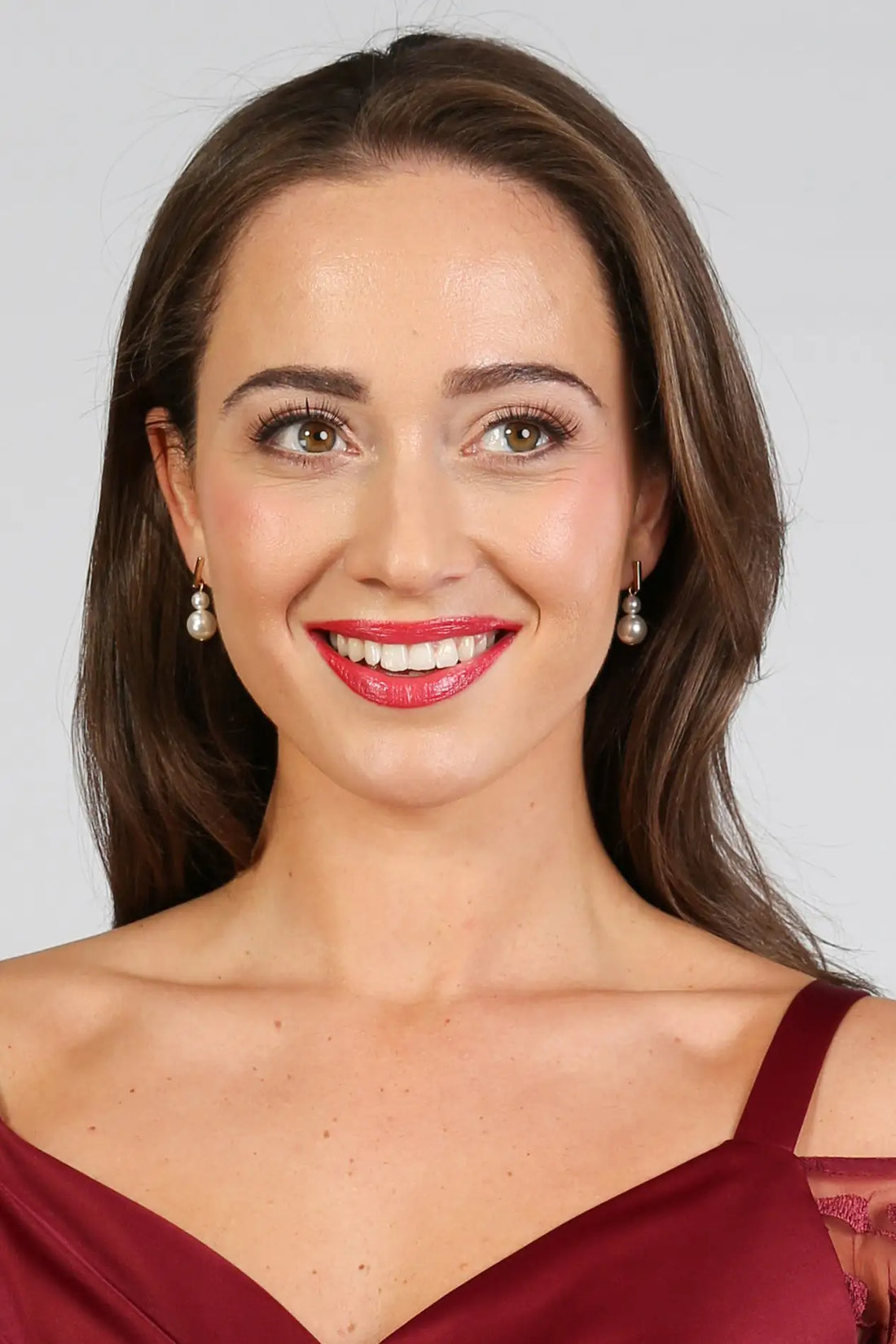 A woman wearing gold bar pearl drop earrings.