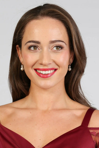 A woman wearing gold bar pearl drop earrings.