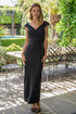 Woman in a black dress standing outdoors with greenery and tables in the background