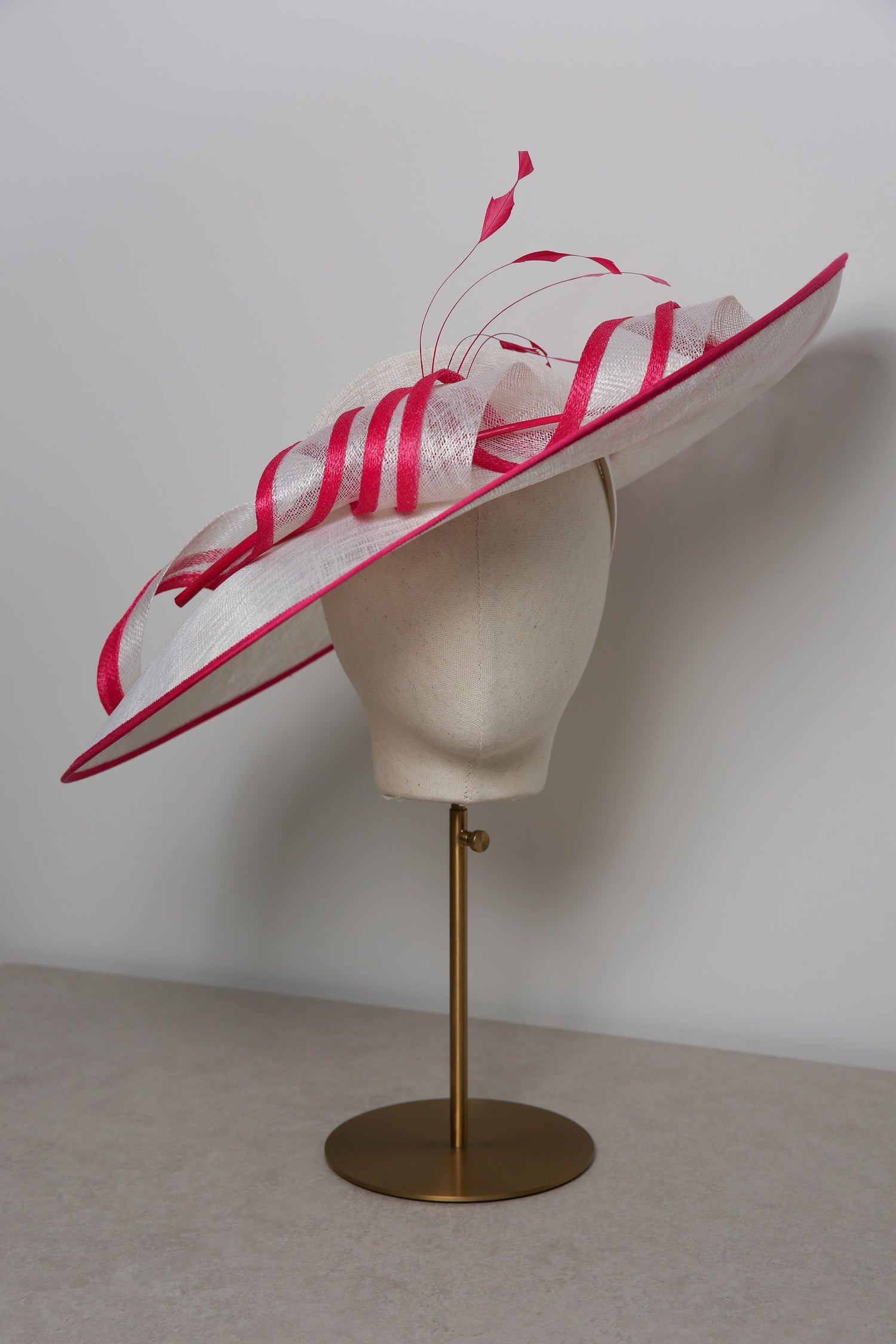 White hat with pink ribbons on a mannequin head against a plain background