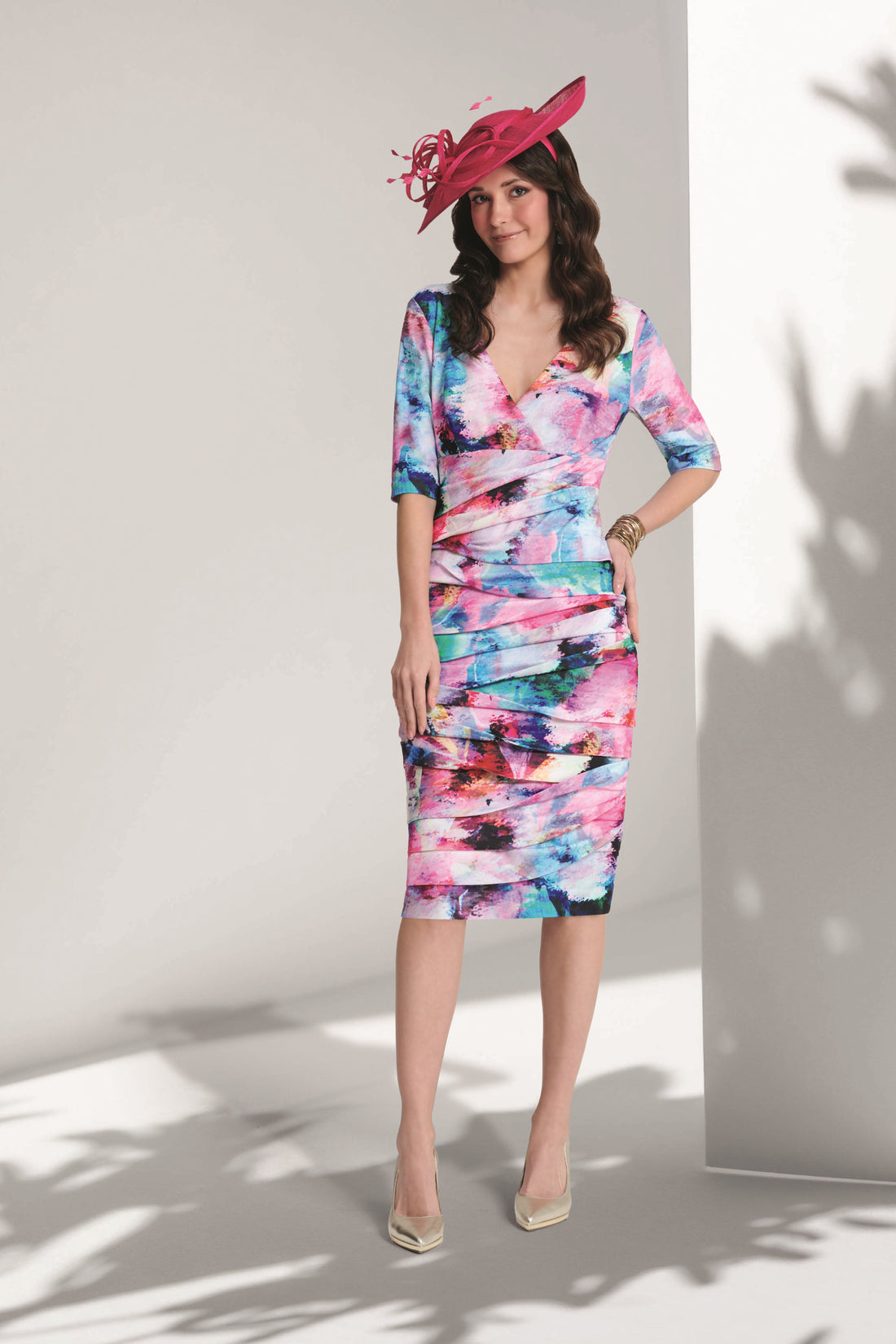 Woman wearing a colorful dress with a pink hat against a white wall