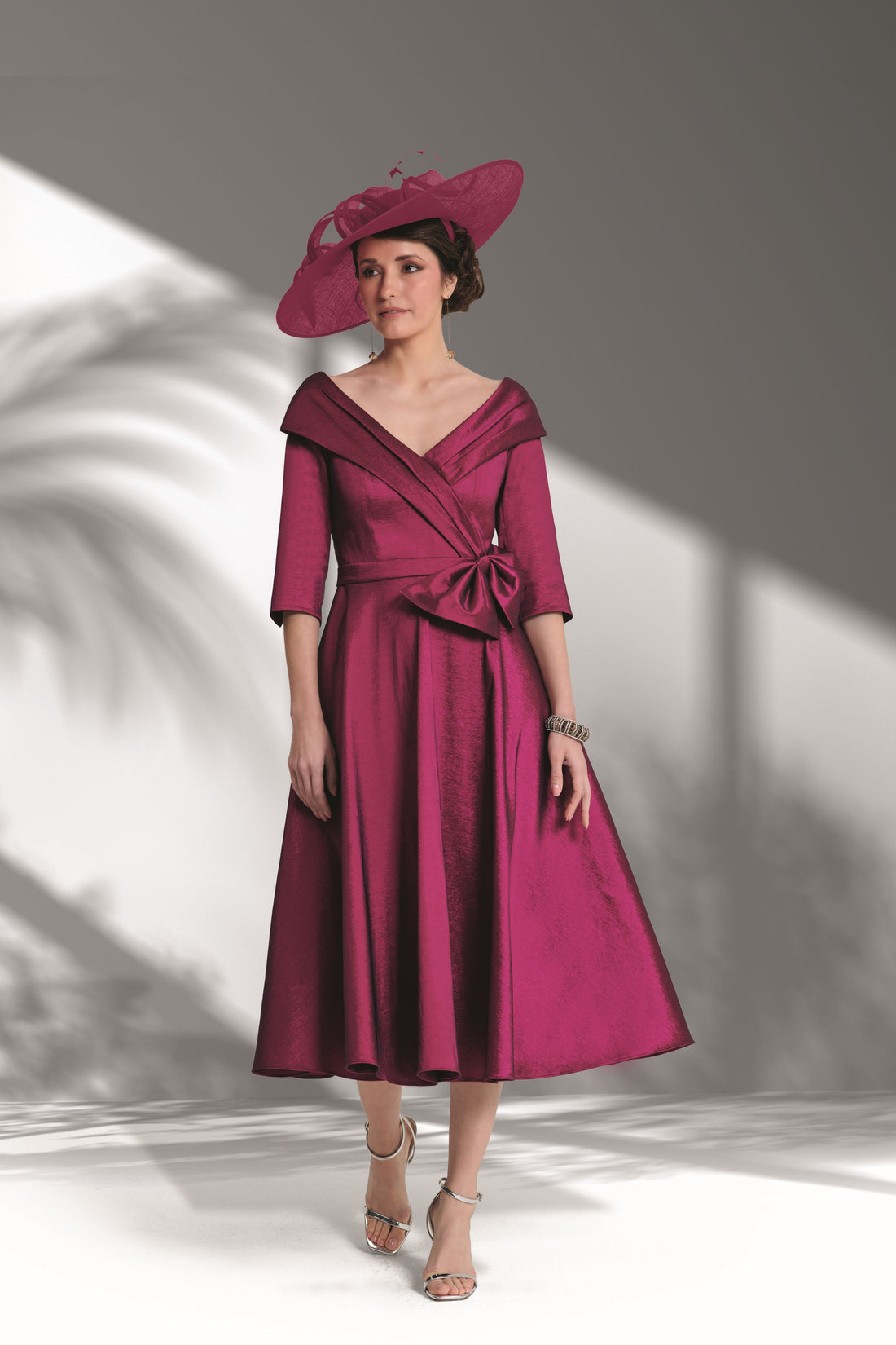 Woman wearing a burgundy dress with a matching hat against a gray background
