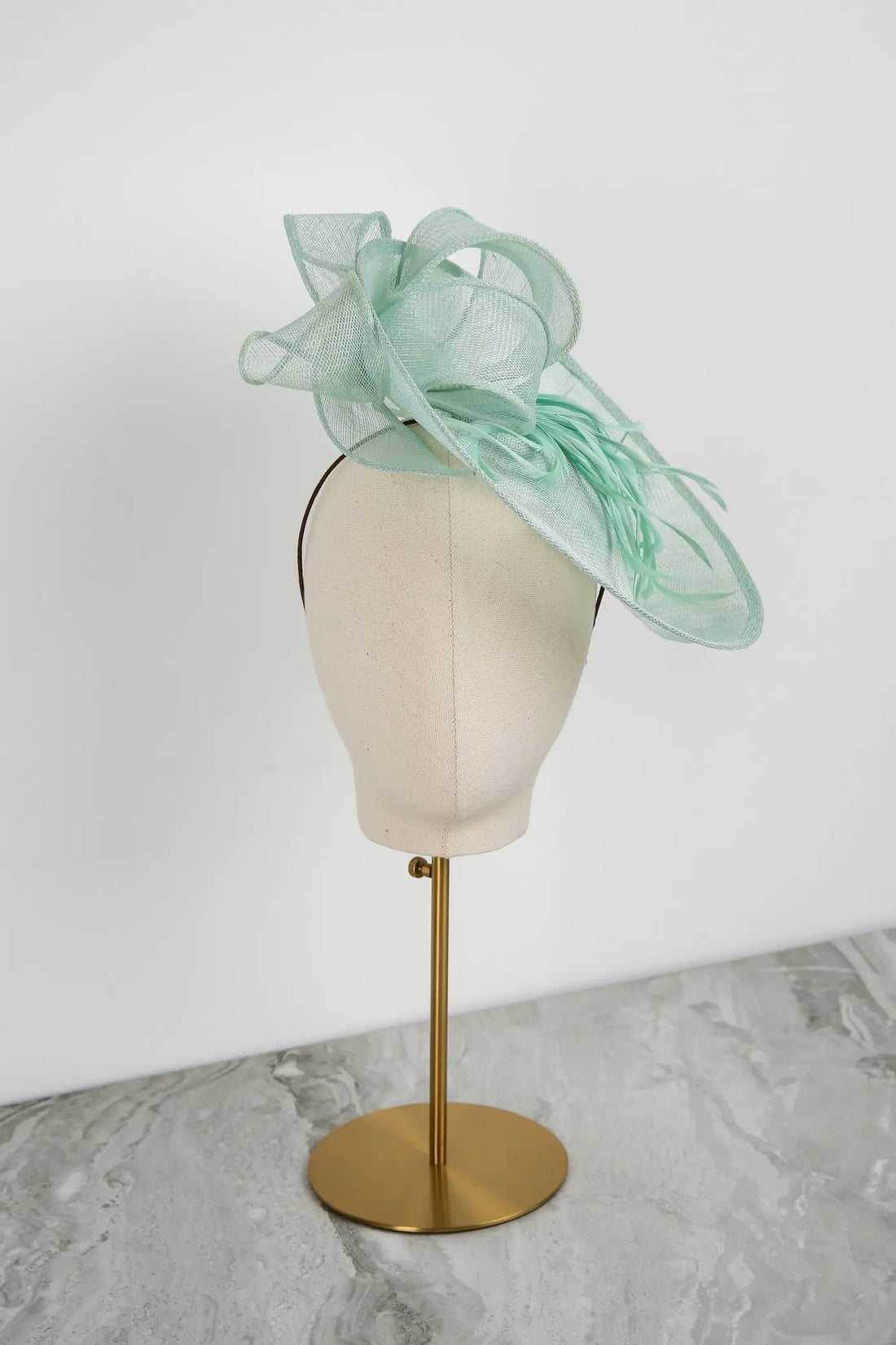 Mint green fascinator on a mannequin head against a white background