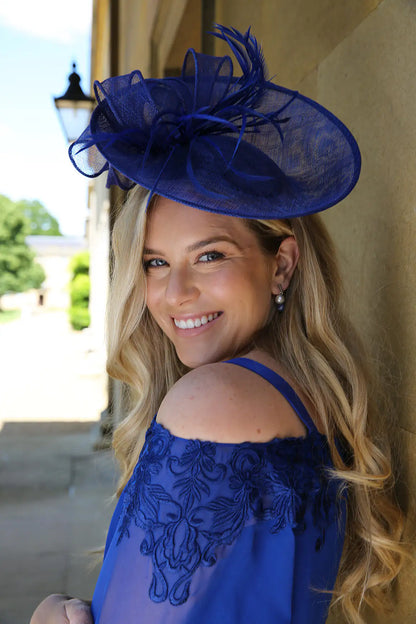 A woman wearing a blue fascinator with a sinamay base and delicate matching feathers.