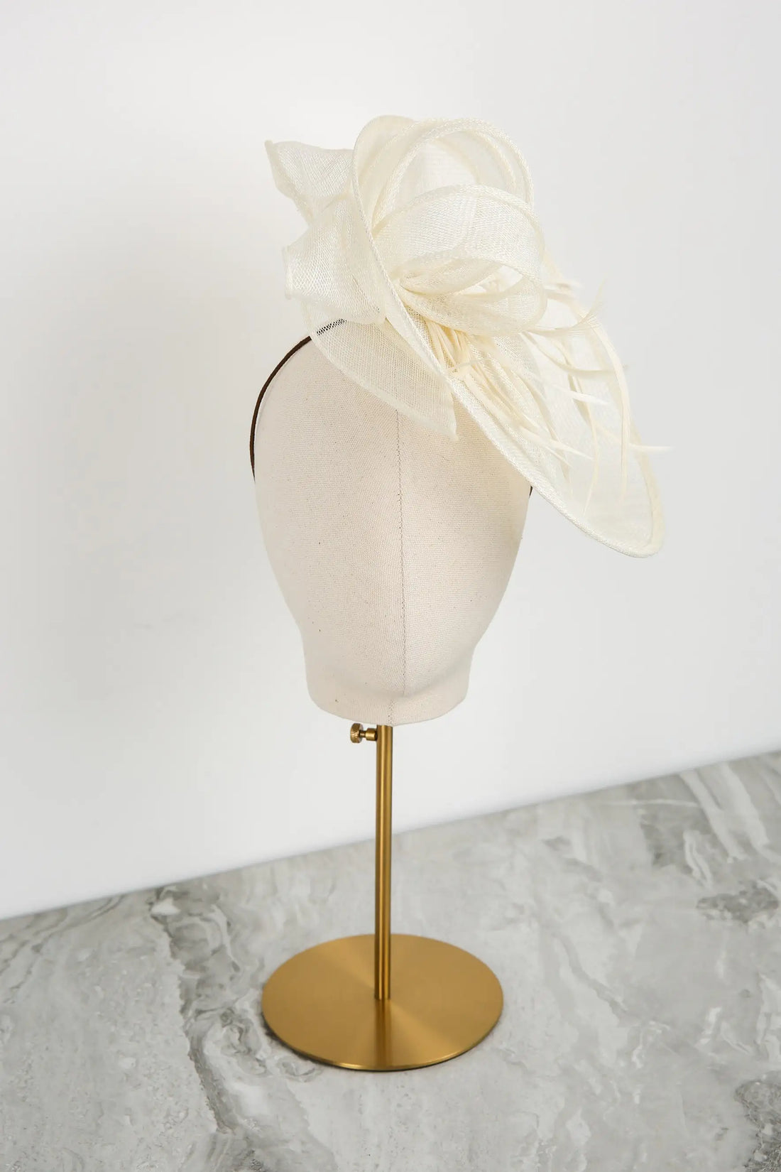 White fascinator on a mannequin head with a gold stand against a white background