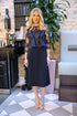 Woman in a Navy lace dress standing in an indoor setting with decorative elements.