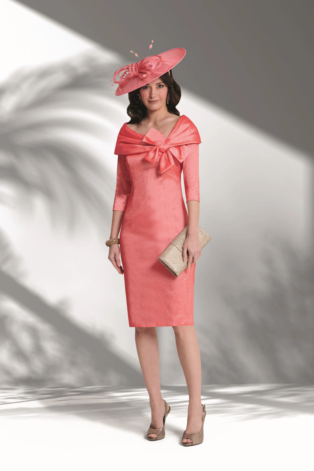 Woman wearing a pink dress with a large bow and matching hat against a white background