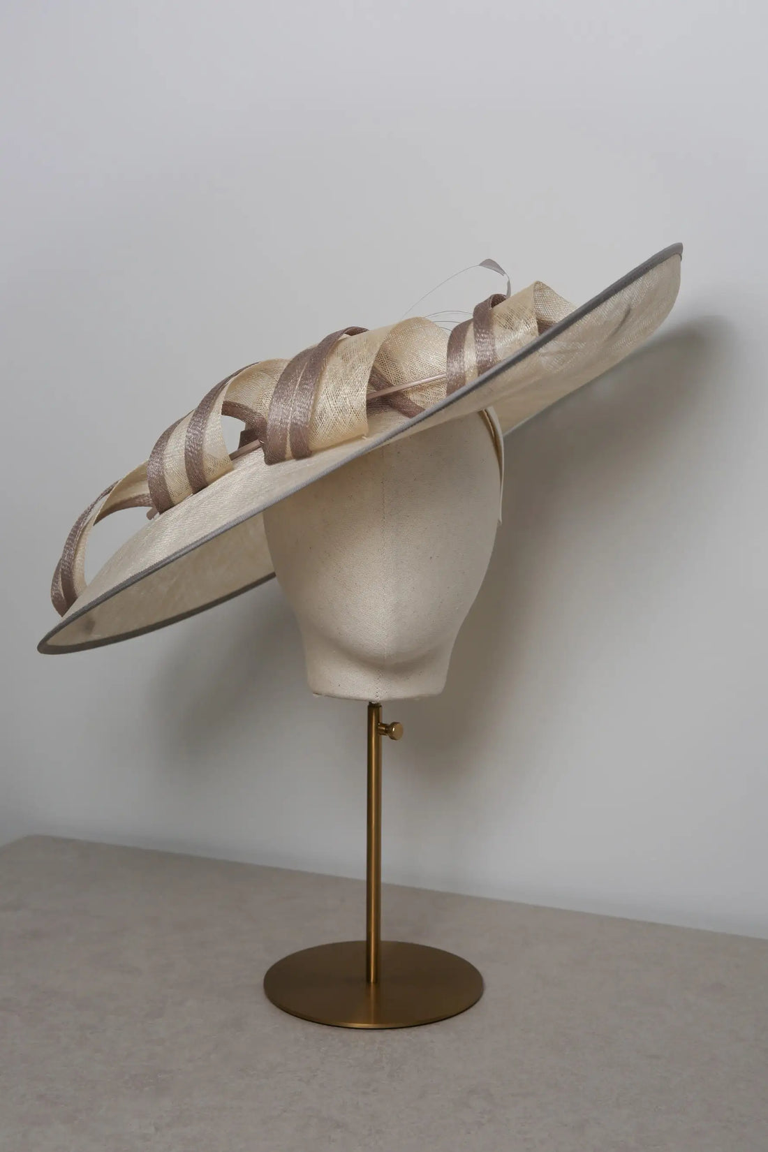Large decorative hat on a mannequin head with a plain background