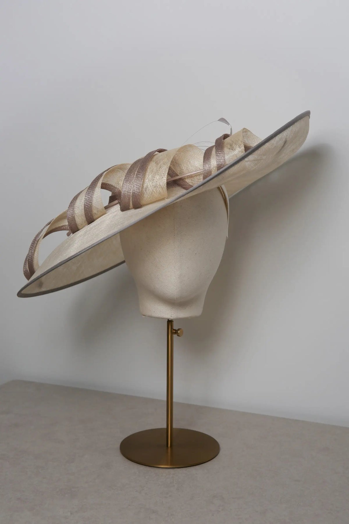 Large decorative hat on a mannequin head with a plain background