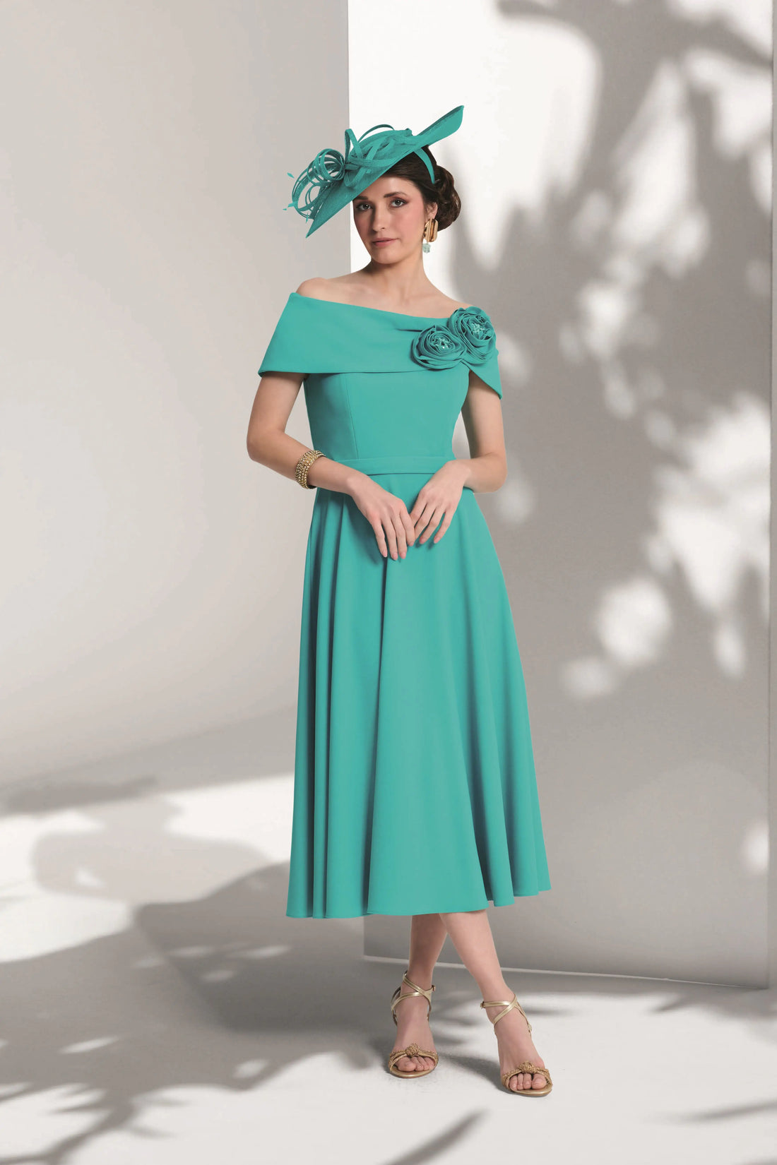 Woman wearing a turquoise off-shoulder dress with floral details against a white background