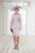 A woman wearing an antique thistle coloured, knee-length stretch taffeta dress with elbow-length sleeves and a hat.