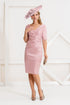A woman wearing a rose blush coloured, knee-length taffeta dress with short sleeves and a V-neckline, accessorised with a hat and heels.