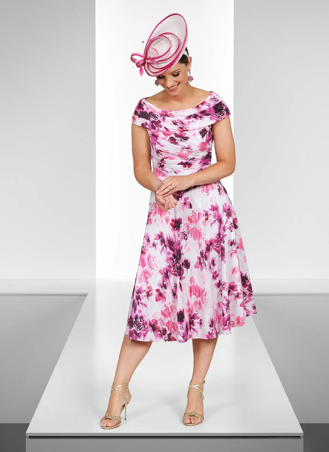 Woman wearing a pink floral dress and matching hat on a white platform.