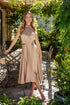 Woman in a beige satin dress standing outdoors with greenery around