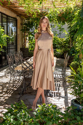 Woman in a beige satin dress standing outdoors with greenery around