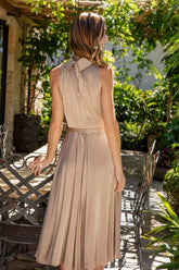 Woman in a beige satin dress standing outdoors with greenery around