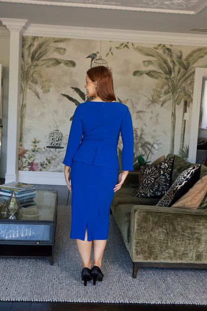 Woman in a blue dress standing in a living room with floral wallpaper.