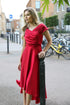 A woman wearing a cherry red silky satin special occasion dress with a flirty high-low hem and pleating.