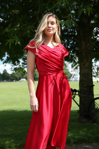 A woman wearing a cherry red silky satin special occasion dress with a flirty high-low hem and pleating.